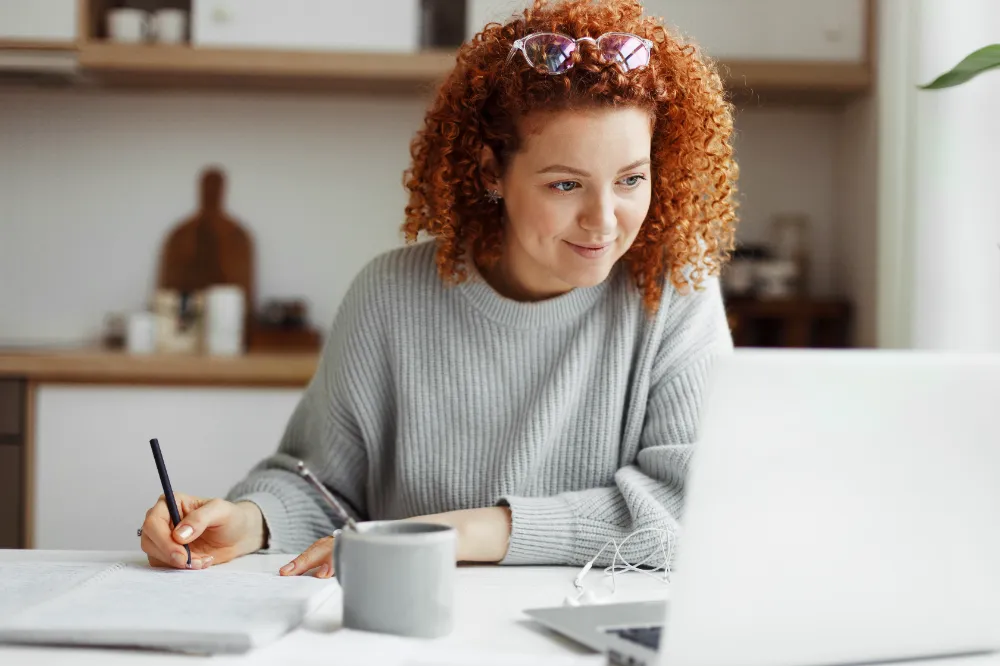 Woman smiling while taking notes during an online consultation, representing Restorations Unlimited’s friendly and no-pressure first step toward planning a home project