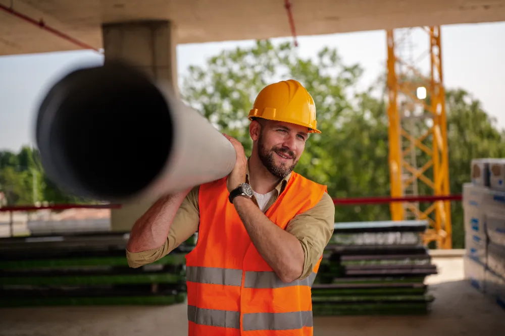 Construction worker carrying a large pipe on-site, representing Restorations Unlimited’s hands-on approach and dedication to helping both new and returning clients build with confidence