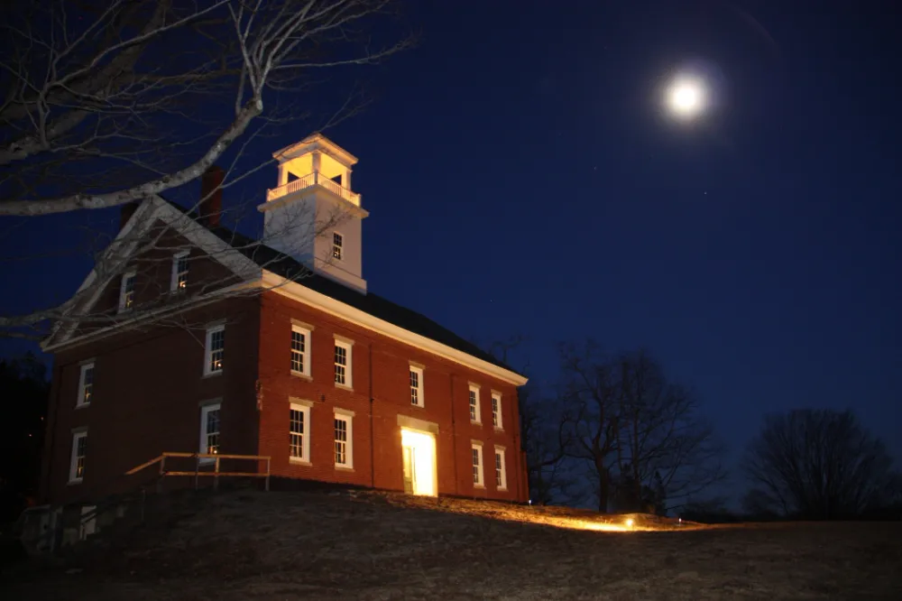 Historic brick commercial building in Maine illuminated at night under a bright moon, representing Restorations Unlimited’s reliable and professional general contractor services for Maine businesses.