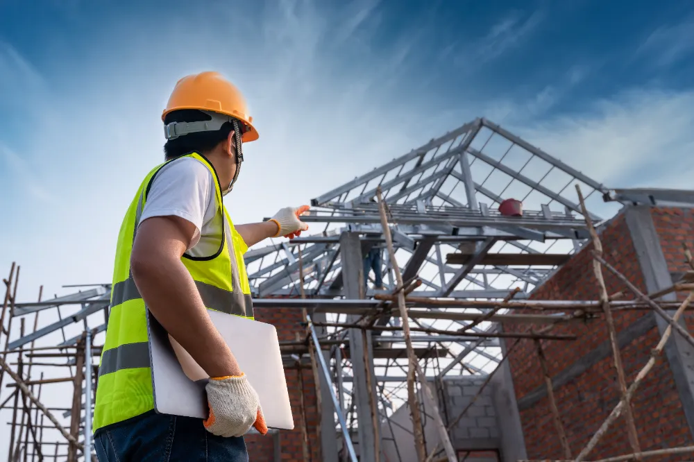 Construction worker wearing a safety vest and hard hat inspecting a steel-frame commercial building addition under a bright sky, representing Restorations Unlimited’s seamless and scalable expansion services for growing businesses.
