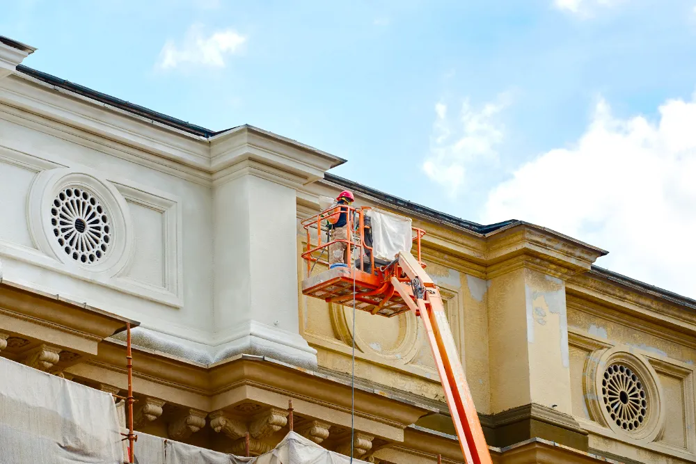 Construction worker on a lift performing exterior renovations on a commercial building facade, representing Restorations Unlimited’s tailored renovation services for Maine businesses focused on quality, compliance, and long-term value.