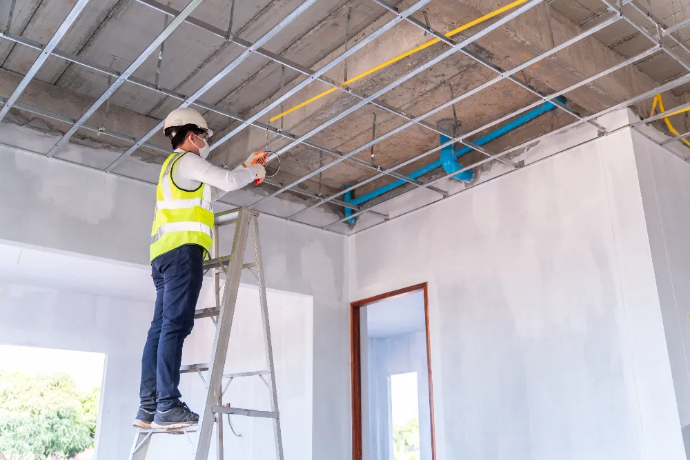 Construction worker on a ladder inspecting ceiling framework inside a commercial building, representing Restorations Unlimited’s commitment to detail, safety, and phased renovation processes that minimize downtime for Maine businesses.