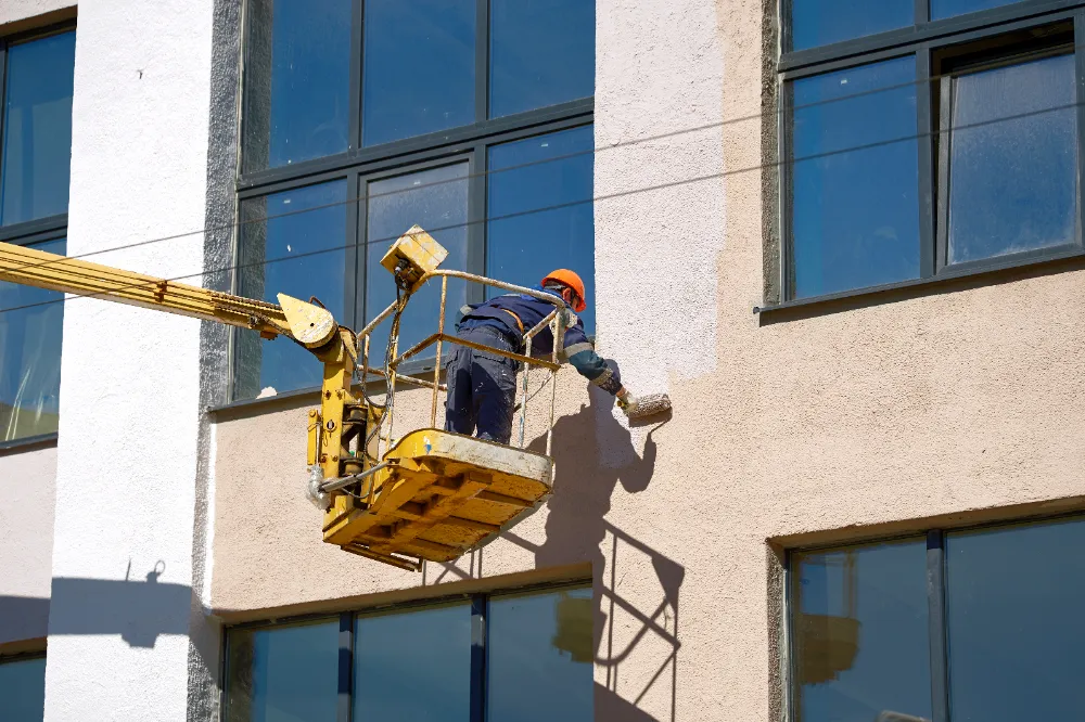Construction worker using a lift to repair and repaint the exterior of a commercial building, representing Restorations Unlimited’s expertise in Maine exterior envelope repairs and weatherproofing solutions for long-term durability.