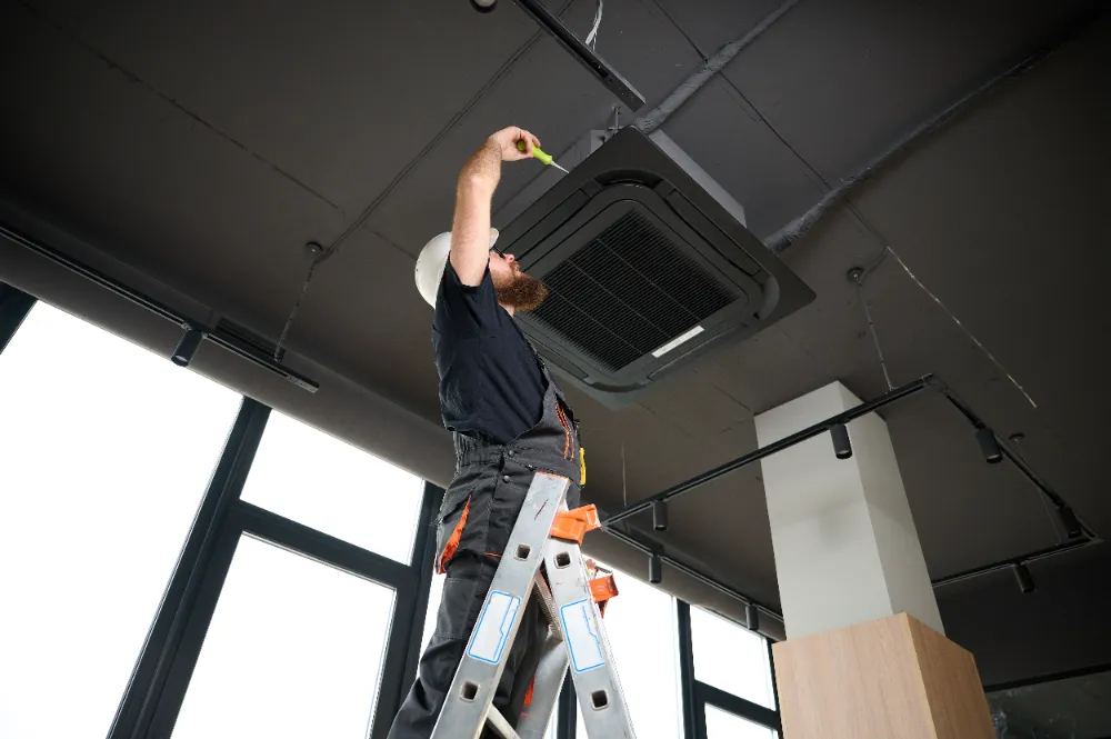 Technician on a ladder repairing a commercial ceiling ventilation system, symbolizing Restorations Unlimited’s commitment to reliable, long-lasting commercial repairs in Maine that minimize downtime and maintain business continuity.