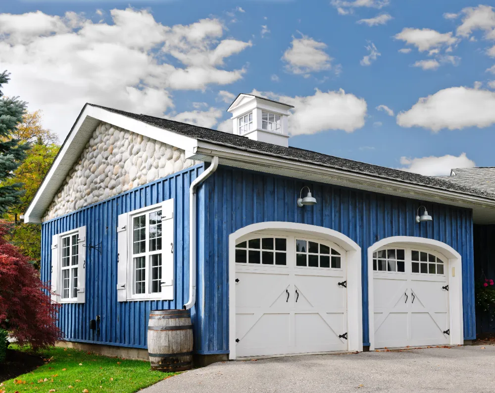 Custom blue barn-style detached garage with white trim and carriage doors—showcasing Restorations Unlimited’s expertise in fully custom garage construction and design across Maine.