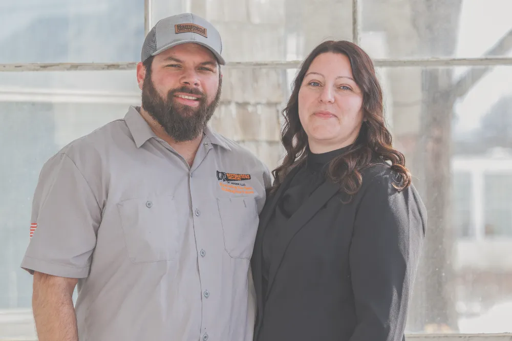Larry and Melinda, husband-and-wife owners of Restorations Unlimited, standing together in front of a workshop window, representing the family-run home remodeling business featured on the About page.