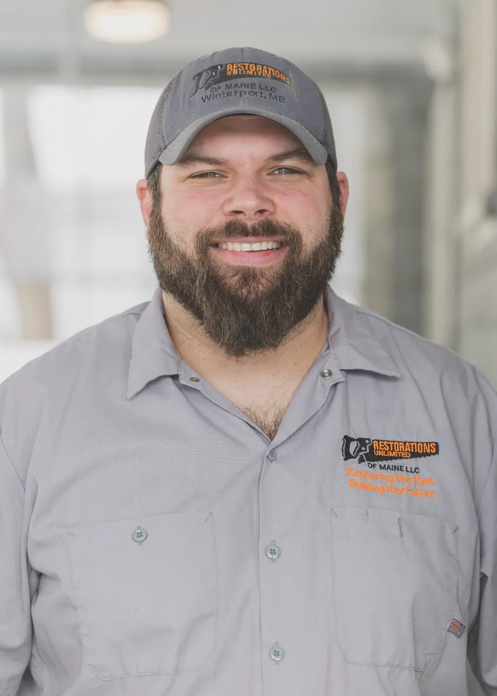 Larry White of Restorations Unlimited smiling in a work shirt and company cap, representing over 30 years of hands-on construction experience and leadership rooted in Maine craftsmanship.