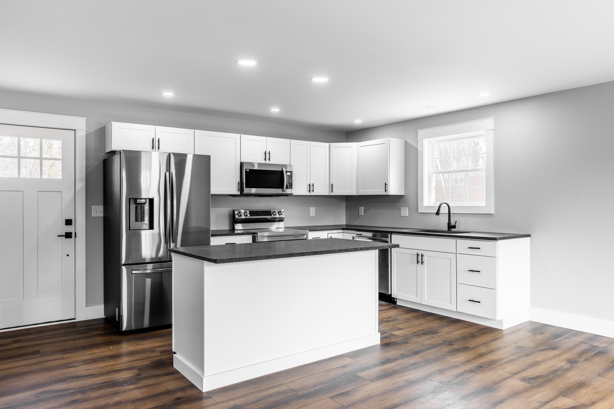 Modern white kitchen with stainless steel appliances and hardwood floors in Blue Hill, Maine, representing Restorations Unlimited’s kitchen remodeling and upgrade services