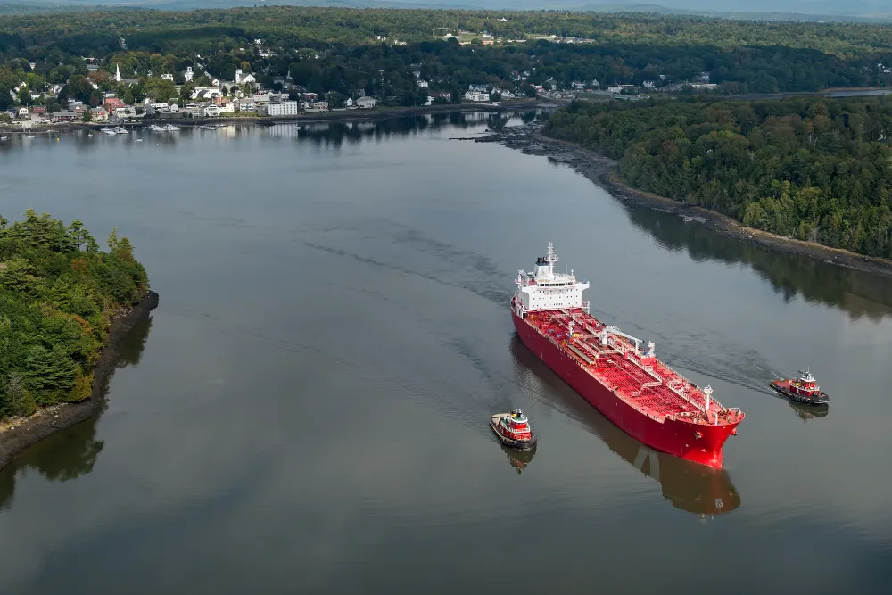 Aerial view of Bucksport, Maine with a red cargo ship on the Penobscot River, representing Restorations Unlimited’s bathroom remodeling services in Bucksport
