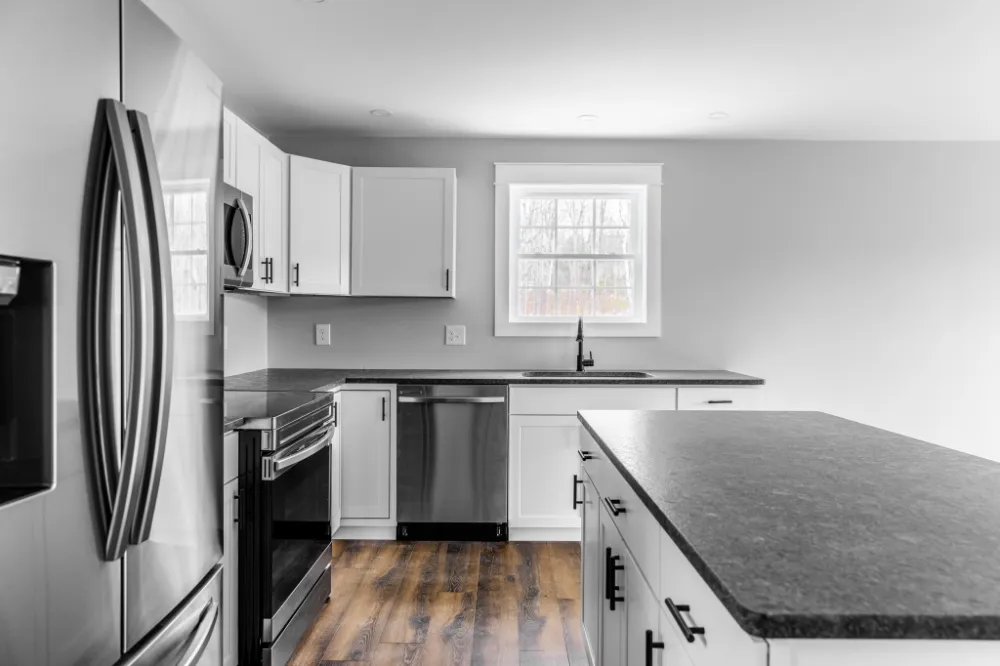 Modern kitchen with white cabinets, black countertops, and stainless steel appliances in Winterport, Maine, representing Restorations Unlimited’s kitchen renovation services