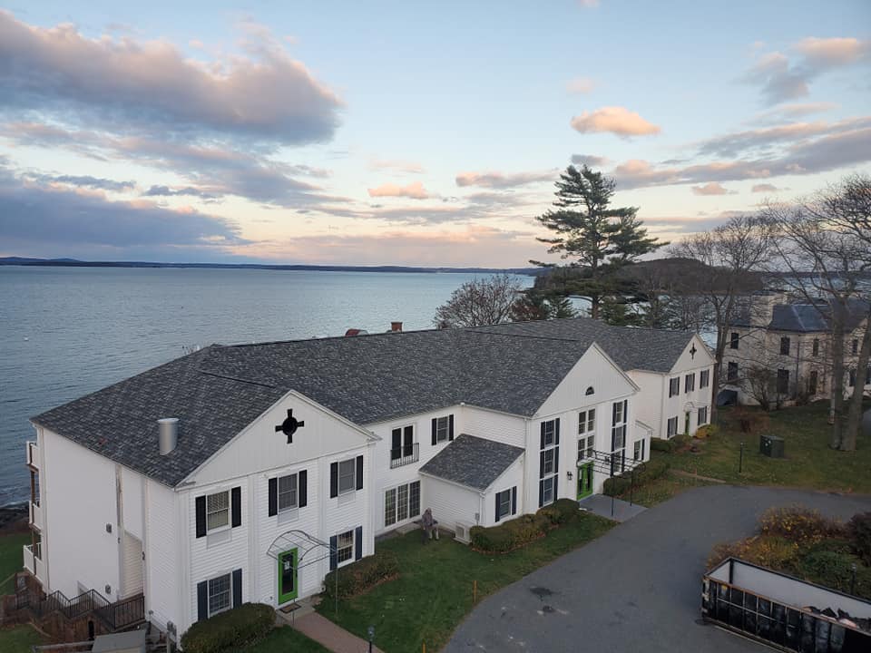 Aerial view of a waterfront commercial building with a newly installed shingle roof in Maine, highlighting Restorations Unlimited’s craftsmanship and long-term roofing solutions designed for durability and coastal weather resistance.