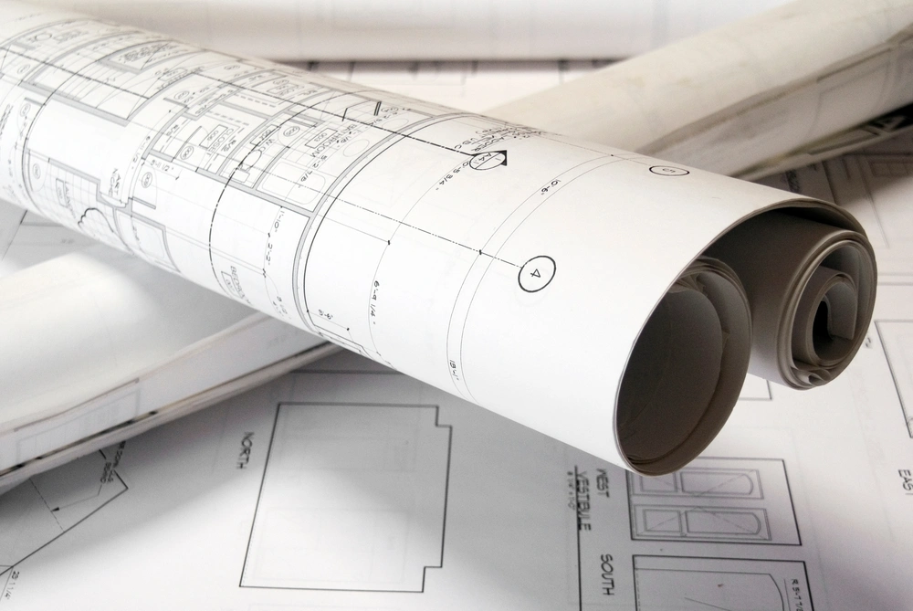 Rolled architectural blueprints on a drafting table—illustrating Restorations Unlimited’s CAD design services in Maine that transform client ideas into precise construction plans and detailed 3D renderings.