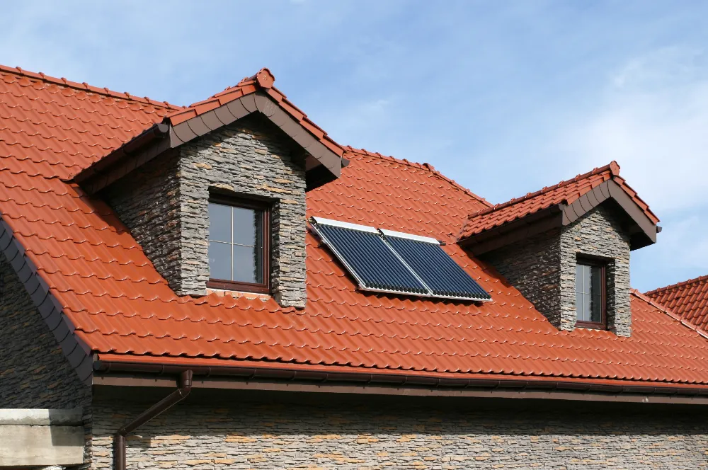 New red tile roof with solar panel installation on a stone-clad home—illustrating Restorations Unlimited’s full-scope roofing services and durable craftsmanship for Maine homeowners.